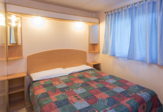 Slaapkamer in mobilhome Camping Solmar - COTTAGE B in Spanje met kleurrijk dekbed en blauwe gordijnen.