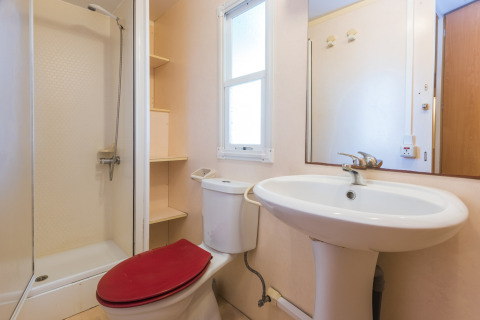 Badeværelse i mobilhome på Camping Solmar med bruser, toilet med rødt sæde og håndvask i Spanien.