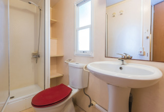 Badkamer in een stacaravan op Camping Solmar, Spanje, met douche, rood toilet en witte wastafel.