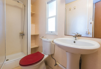 Bagno di una casa mobile al Camping Solmar, Spagna, con doccia, WC rosso e lavabo bianco.