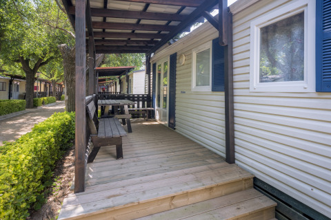 Træterrasse med bænk og bord foran en mobilhome ved Camping Solmar - COTTAGE B i Spanien en solrig dag.