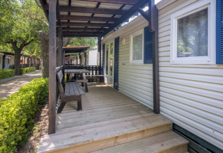 Houten veranda met zitbank en tafel bij een stacaravan op Camping Solmar - COTTAGE B in Spanje.