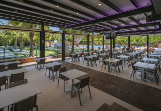 Overdekte eetruimte bij Camping Solmar - COTTAGE B in Spanje met uitzicht op zwembad en ligbedden.