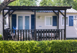 Stacaravan met overdekte veranda en blauwe luiken bij Camping Solmar COTTAGE B, achter groen hegje in Spanje.