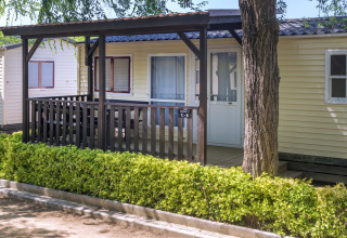 Mobilhome med veranda og hæk foran, Camping Solmar - COTTAGE B, set i solskin i Spanien