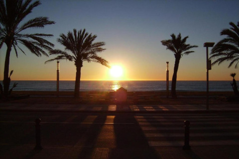 Zonsondergang boven zee vanaf Camping Solmar - COTTAGE B in Spanje, met palmbomen en boulevard.
