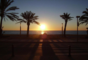 Tramonto sul mare visto da Camping Solmar - COTTAGE B in Spagna, con palme e passeggiata sul lungomare.