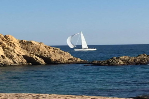 Et billede taget fra Camping Solmar - COTTAGE B i Spanien med udsigt til klipper og en sejlbåd til havs.