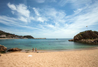 Uitzicht vanaf Camping Solmar - COTTAGE B in Spanje: zandstrand, kalme zee, rotsen en blauwe lucht.