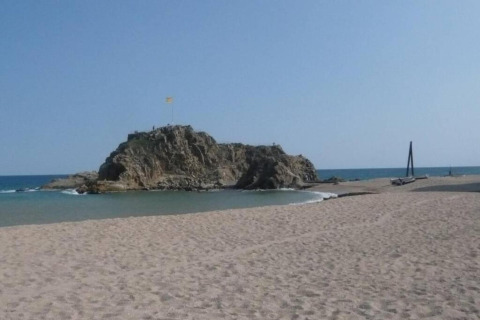 Strandbillede fra Camping Solmar - COTTAGE B i Spanien, med sand, hav og en klippeø i baggrunden.