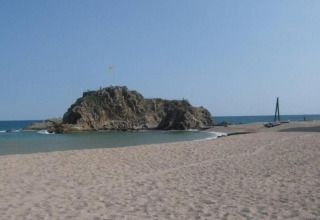 Strandzicht bij Camping Solmar - COTTAGE B in Spanje, met zand, zee en een rotsachtig eiland op de achtergrond.