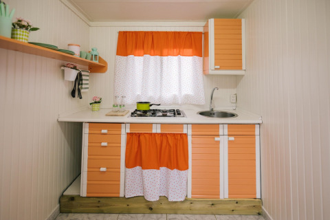 Kleine keuken van een stacaravan met oranje-witte kasten en gordijnen in Miramar Mobile home CINQUE TERRE, Spanje.