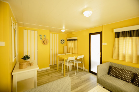 Lichte, gezellige woonkamer in de Miramar Mobile home CINQUE TERRE met gele muren en eethoek.