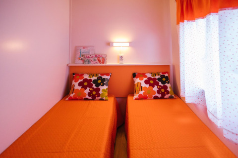Twee eenpersoonsbedden met oranje dekens en bloemenkussens in Miramar Mobile Home CINQUE TERRE in Spanje.