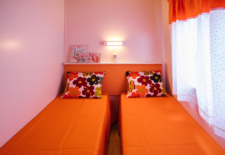 Twee eenpersoonsbedden met oranje dekens en bloemenkussens in Miramar Mobile Home CINQUE TERRE in Spanje.