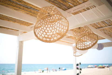 Rieten lampen hangen aan een houten pergola met uitzicht op het strand bij Miramar Mobile Home in Spanje.