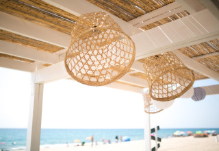 Rieten lampen hangen aan een houten pergola met uitzicht op het strand bij Miramar Mobile Home in Spanje.