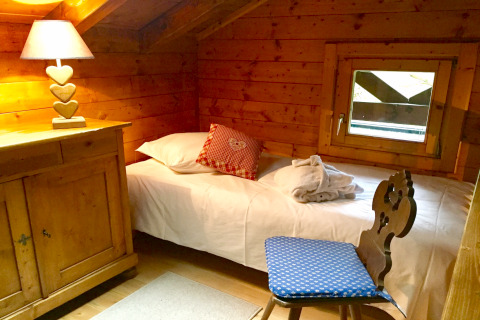 Chambre chaleureuse avec murs en bois, lit simple, lampe à cœur et fenêtre au chalet Remschweiler, France.