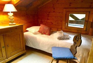 Chambre chaleureuse avec murs en bois, lit simple, lampe à cœur et fenêtre au chalet Remschweiler, France.