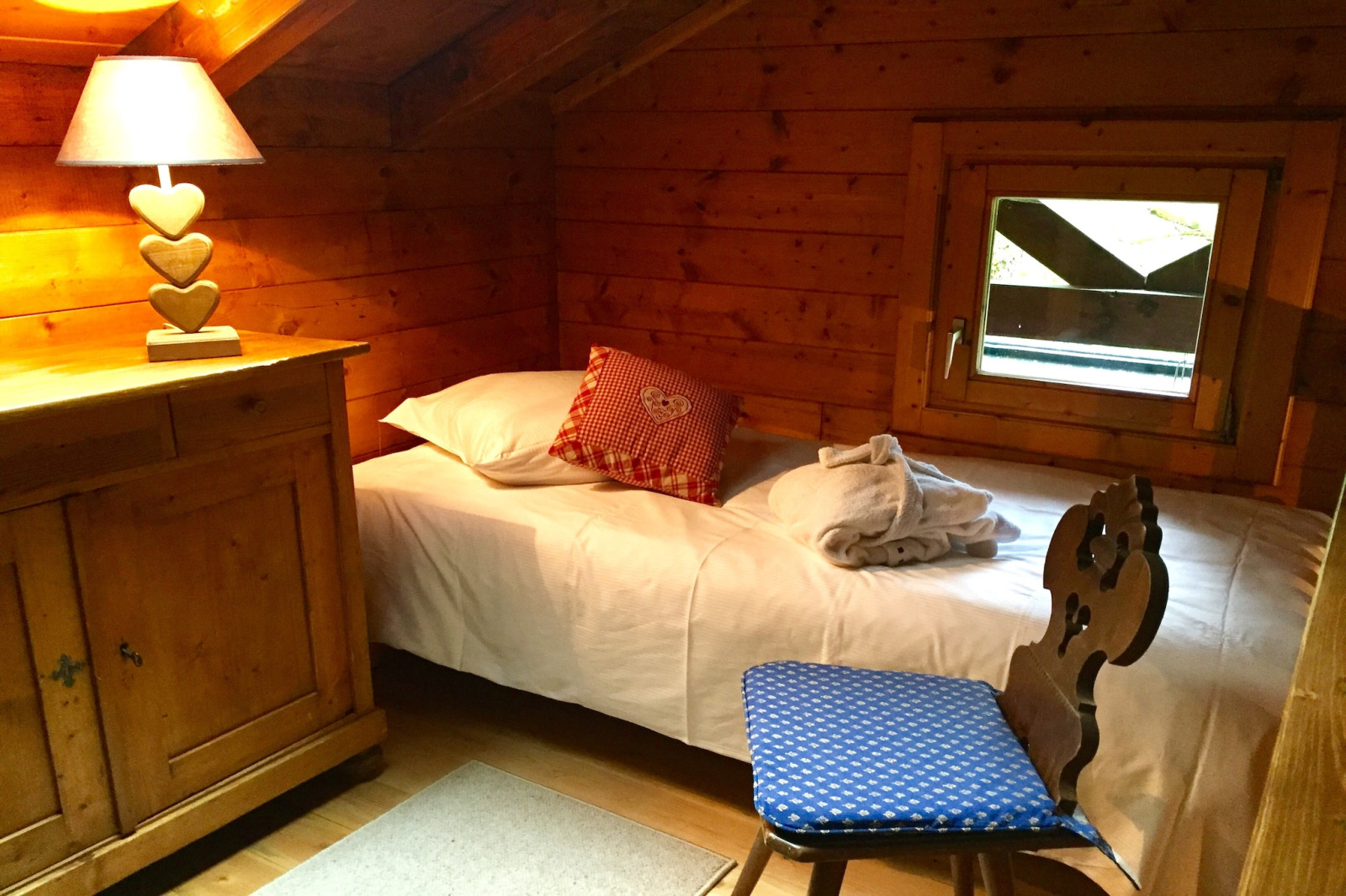 Gezellige slaapkamer met houten wanden, eenpersoonsbed, hartjeslamp en raam in chalet Remschweiler, Frankrijk.