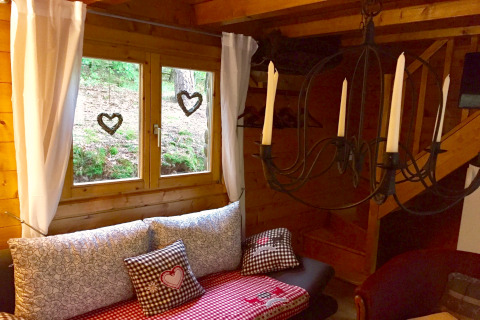 Coin douillet dans le chalet Remschweiler en France, avec fenêtre, coussins, rideaux blancs et lustre à bougies.
