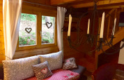 Hyggelig hjørne i chalet Remschweiler i Frankrig, med vindue, gardiner, puder og smedejernslysestage.