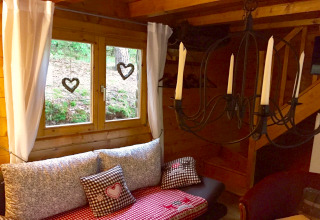 Coin douillet dans le chalet Remschweiler en France, avec fenêtre, coussins, rideaux blancs et lustre à bougies.