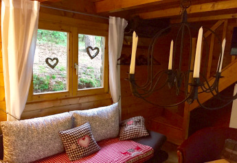 Hyggelig hjørne i chalet Remschweiler i Frankrig, med vindue, gardiner, puder og smedejernslysestage.