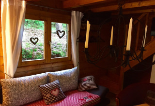 Gezellige hoek in chalet Remschweiler in Frankrijk, met raam, kussens, witte gordijnen en ijzeren kandelaar.