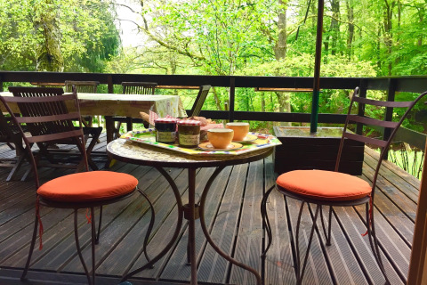 Buitenterras bij chalet Remschweiler in Frankrijk met stoelen, tafel, jam en omringd door groen bos.