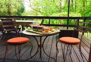 Buitenterras bij chalet Remschweiler in Frankrijk met stoelen, tafel, jam en omringd door groen bos.
