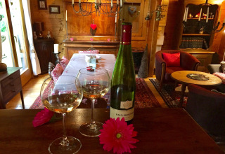 Twee wijnglazen en een fles wijn op een houten tafel in een gezellig chalet in Remschweiler, Frankrijk.
