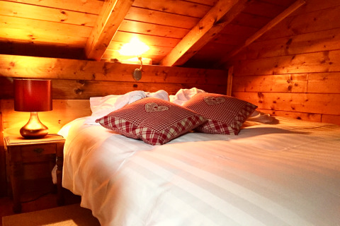 Chambre chaleureuse d’un chalet en France, avec murs en bois, lit double et coussins rouges à carreaux.