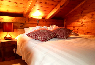 Chambre chaleureuse d’un chalet en France, avec murs en bois, lit double et coussins rouges à carreaux.