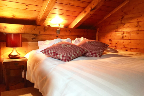 Gezellige slaapkamer in een chalet in Frankrijk met houten wanden, wit beddengoed en rode kussens.
