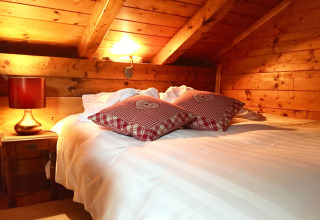Gezellige slaapkamer in een chalet in Frankrijk met houten wanden, wit beddengoed en rode kussens.