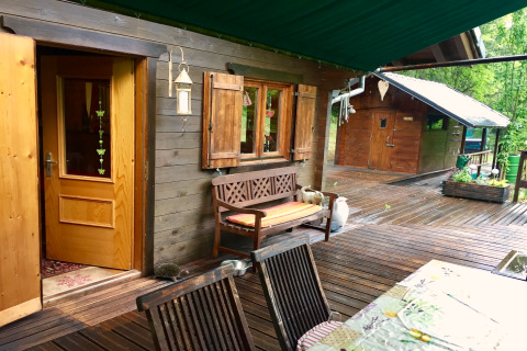 Vue du chalet Remschweiler en France, terrasse en bois, banc, fenêtres ouvertes et verdure luxuriante.