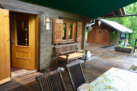 Uitzicht op chalet Remschweiler in Frankrijk met houten terras, bank, open ramen en groene omgeving.
