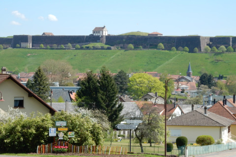 Uitzicht vanaf chalet Remschweiler in Frankrijk met dorpshuizen, groene heuvels en een oude vesting op de achtergrond.