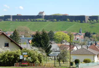 Uitzicht vanaf chalet Remschweiler in Frankrijk met dorpshuizen, groene heuvels en een oude vesting op de achtergrond.