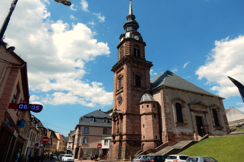 Photo d'une église historique à Remschweiler, France, sous un ciel bleu parsemé de quelques nuages.