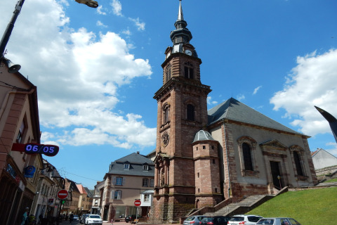 Foto van een historische kerk in Remschweiler, Frankrijk, met blauwe lucht en enkele wolken.