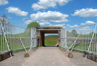 Toegangspoort met metalen hekken bij chalet Remschweiler in Frankrijk, met groen en blauwe lucht.