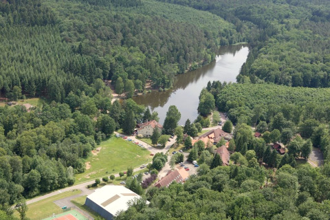 Vue aérienne du chalet Remschweiler en France, entouré de forêt dense et d’une rivière sinueuse paisible.