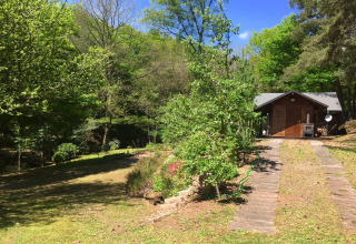 Houten chalet genaamd Remschweiler in Frankrijk, omringd door groene bomen onder een blauwe lucht.