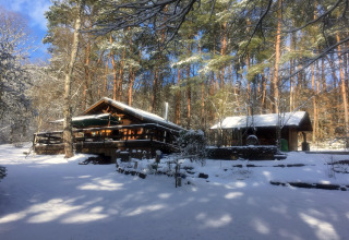 Chalet Remschweiler en France recouvert de neige, entouré de forêt sous un ciel bleu clair d’hiver.