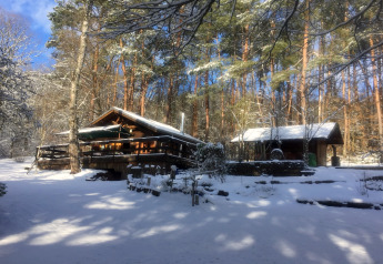 Træchalet Remschweiler i Frankrig dækket af sne, omgivet af skov under en klar blå vinterhimmel.
