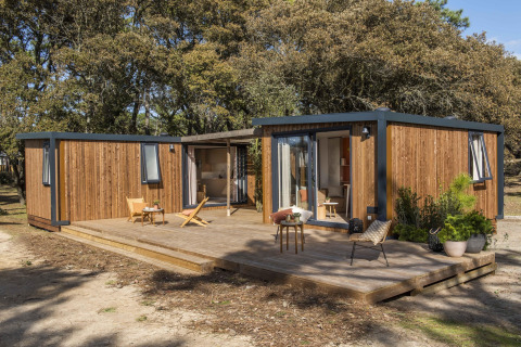Et moderne feriehus med træbeklædning og stor terrasse ved Beach Resort Agde 5, omgivet af træer.