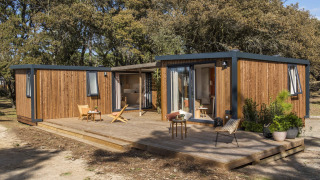 Et moderne feriehus med træbeklædning og stor terrasse ved Beach Resort Agde 5, omgivet af træer.