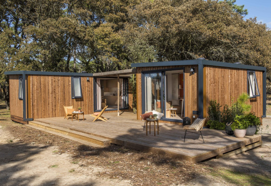 Et moderne feriehus med træbeklædning og stor terrasse ved Beach Resort Agde 5, omgivet af træer.